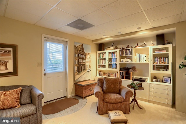 living area with a drop ceiling and light colored carpet