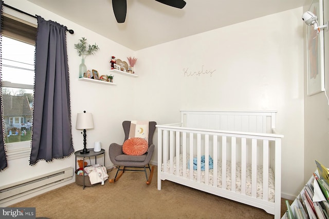 carpeted bedroom with baseboard heating, ceiling fan, and a crib