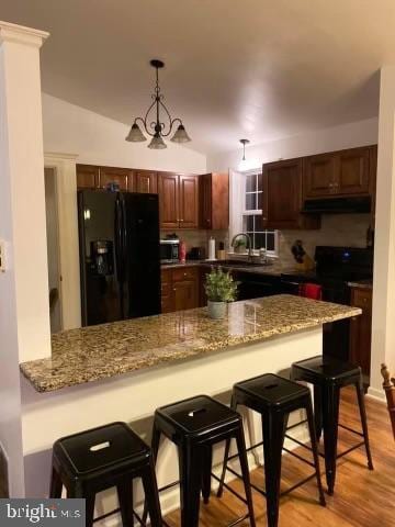 kitchen with kitchen peninsula, vaulted ceiling, black appliances, pendant lighting, and light hardwood / wood-style floors