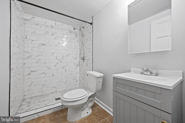 bathroom with tiled shower, tile patterned flooring, vanity, and toilet