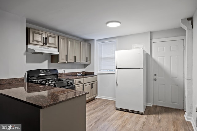 kitchen featuring white refrigerator, black gas stove, dark stone countertops, light hardwood / wood-style floors, and kitchen peninsula