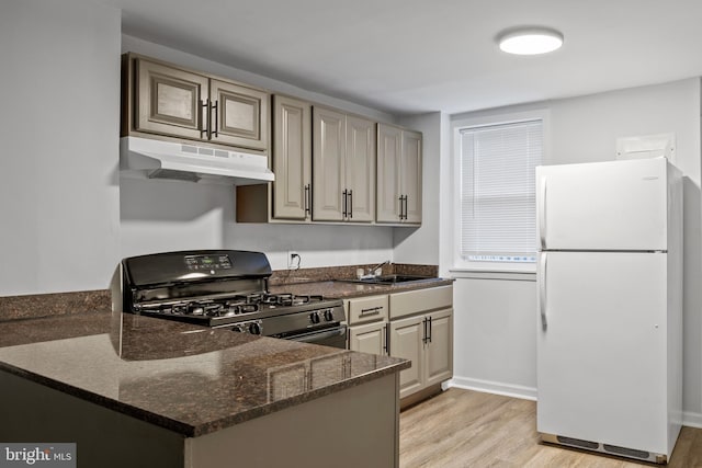 kitchen with dark stone counters, black range with gas stovetop, light hardwood / wood-style floors, white fridge, and kitchen peninsula