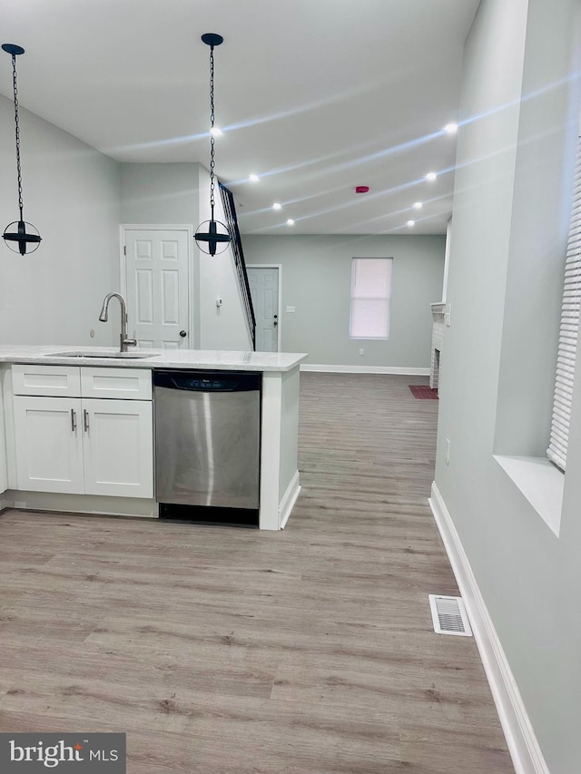 kitchen with light wood-type flooring, stainless steel dishwasher, sink, white cabinets, and hanging light fixtures