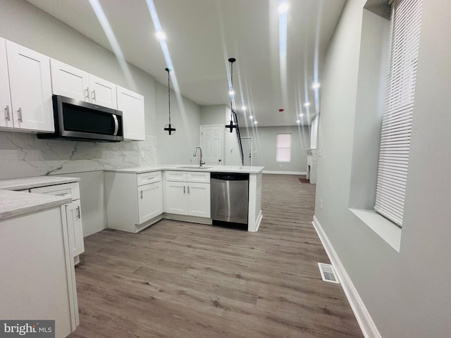 kitchen featuring sink, stainless steel appliances, light hardwood / wood-style floors, pendant lighting, and white cabinets