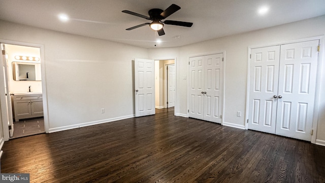 unfurnished bedroom featuring ceiling fan, connected bathroom, two closets, and dark hardwood / wood-style floors