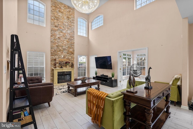 living room featuring a stone fireplace, a high ceiling, and a notable chandelier