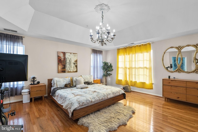 bedroom with a raised ceiling, a chandelier, and hardwood / wood-style flooring