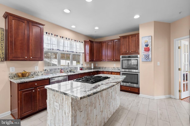 kitchen featuring light stone countertops, appliances with stainless steel finishes, a kitchen island, and sink