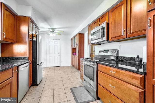 kitchen with ceiling fan, light tile patterned floors, stainless steel appliances, and dark stone counters