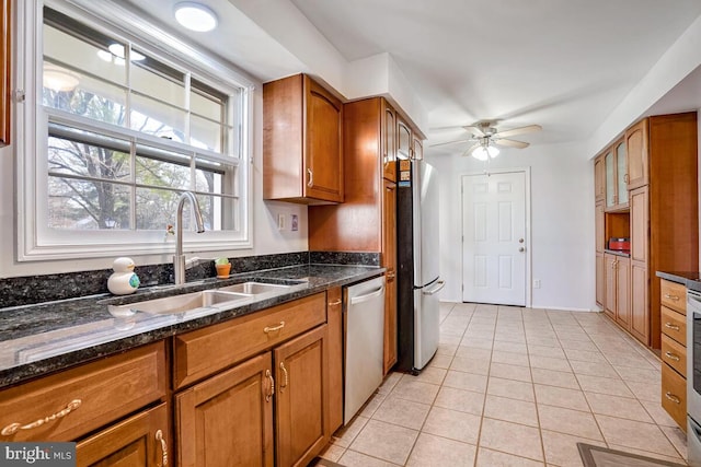 kitchen with sink, ceiling fan, dark stone countertops, light tile patterned flooring, and stainless steel appliances