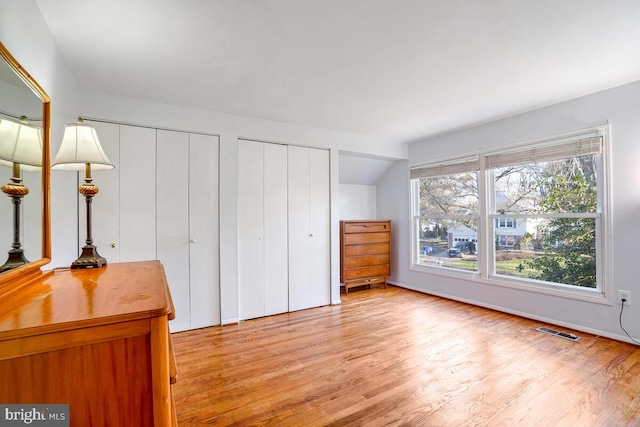 unfurnished bedroom with vaulted ceiling, light wood-type flooring, and two closets