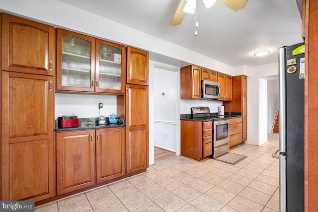 kitchen with dark stone counters, ceiling fan, light tile patterned floors, and stainless steel appliances