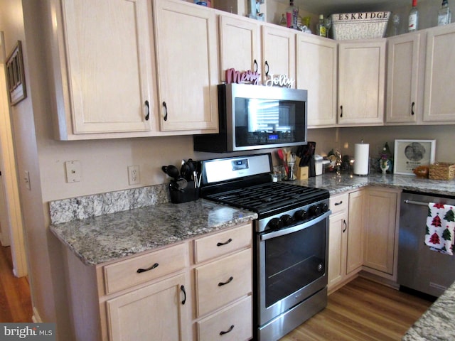 kitchen with light stone countertops, appliances with stainless steel finishes, light hardwood / wood-style flooring, and light brown cabinetry