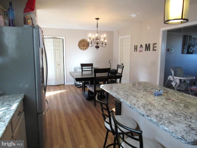 kitchen featuring a kitchen bar, stainless steel fridge, light stone counters, wood-type flooring, and a notable chandelier