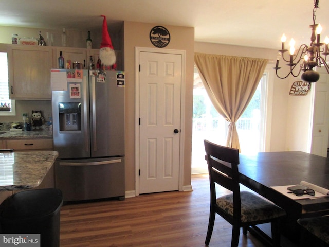 kitchen with stainless steel fridge with ice dispenser, light stone counters, a notable chandelier, wood-type flooring, and light brown cabinetry