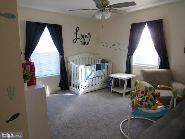 carpeted bedroom featuring ceiling fan and a crib