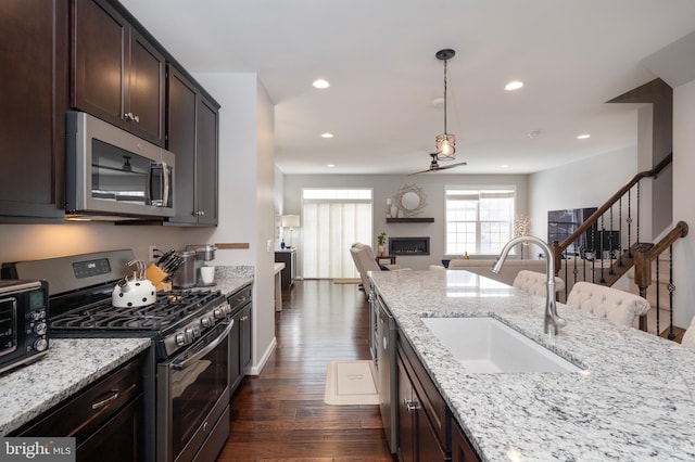 kitchen featuring sink, stainless steel appliances, dark brown cabinetry, and light stone countertops