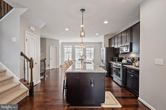 kitchen with a kitchen bar, stainless steel appliances, an island with sink, sink, and hanging light fixtures