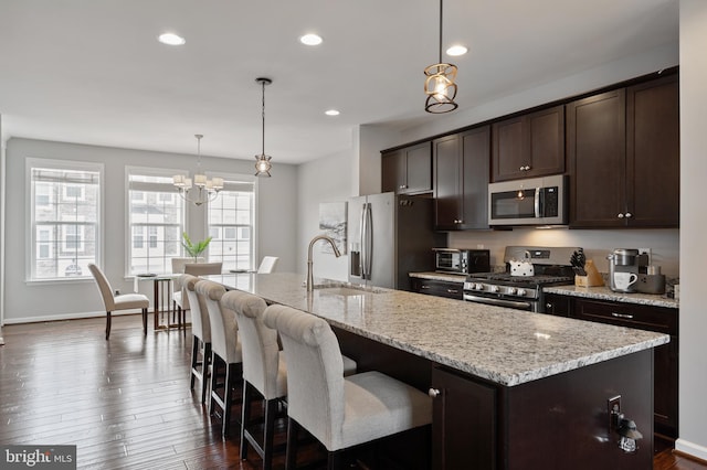 kitchen featuring appliances with stainless steel finishes, an island with sink, sink, hanging light fixtures, and dark brown cabinets