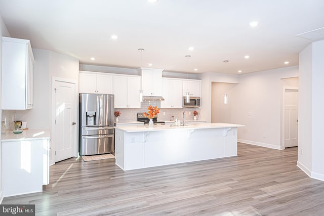 kitchen featuring an island with sink, hanging light fixtures, light wood-type flooring, and appliances with stainless steel finishes