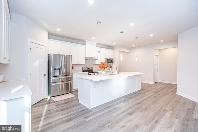 kitchen with a center island with sink, white cabinets, light wood-type flooring, appliances with stainless steel finishes, and decorative light fixtures