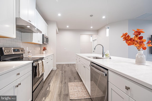 kitchen with white cabinets, sink, appliances with stainless steel finishes, decorative light fixtures, and light hardwood / wood-style floors