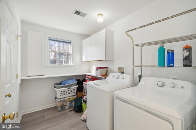 clothes washing area with separate washer and dryer, light hardwood / wood-style flooring, and cabinets