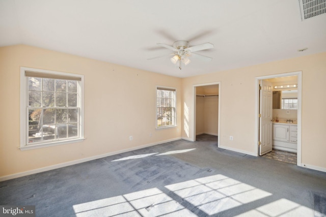 unfurnished bedroom featuring carpet, a walk in closet, ensuite bathroom, ceiling fan, and a closet