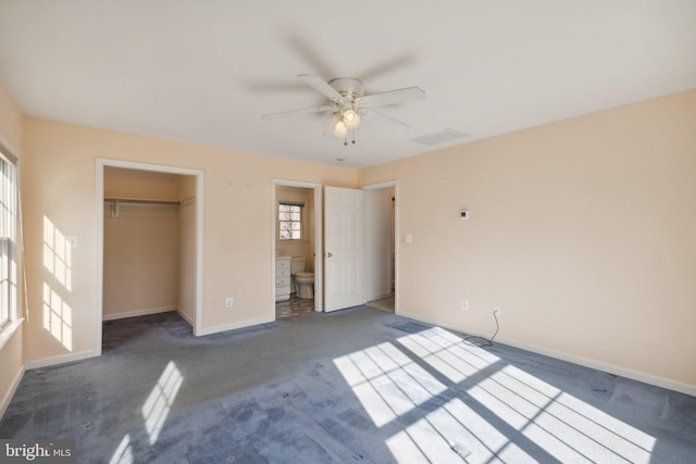 unfurnished bedroom with ensuite bath, ceiling fan, dark colored carpet, a walk in closet, and a closet