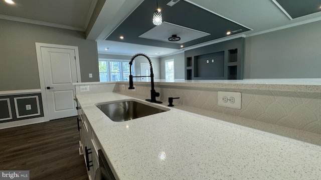 kitchen with light stone counters, ornamental molding, dark wood-type flooring, sink, and pendant lighting