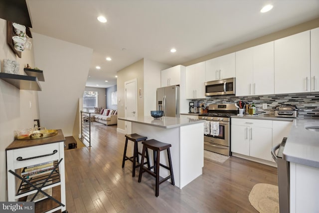 kitchen featuring a breakfast bar, stainless steel appliances, a center island, dark hardwood / wood-style floors, and white cabinetry