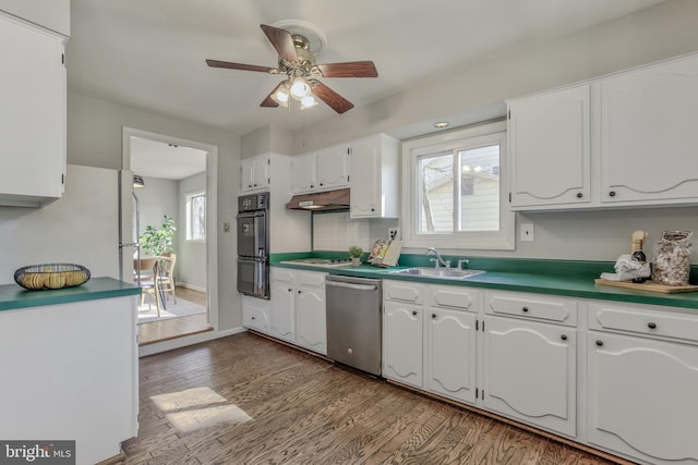 kitchen featuring white cabinets, dishwasher, wood finished floors, under cabinet range hood, and a sink