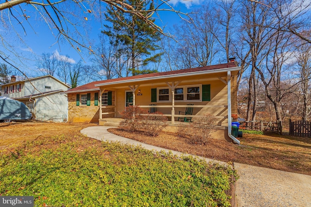 ranch-style home with brick siding, a chimney, covered porch, a front yard, and fence