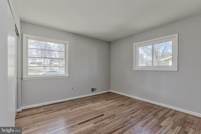 empty room with wood finished floors, visible vents, and baseboards