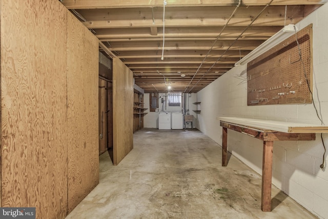 unfinished basement featuring concrete block wall, electric panel, and washer and clothes dryer