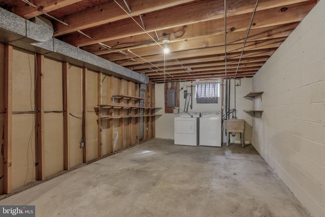 basement featuring concrete block wall, electric panel, washer and clothes dryer, and a sink