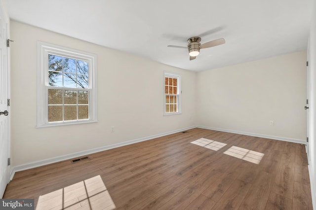 empty room with ceiling fan, visible vents, baseboards, and wood finished floors