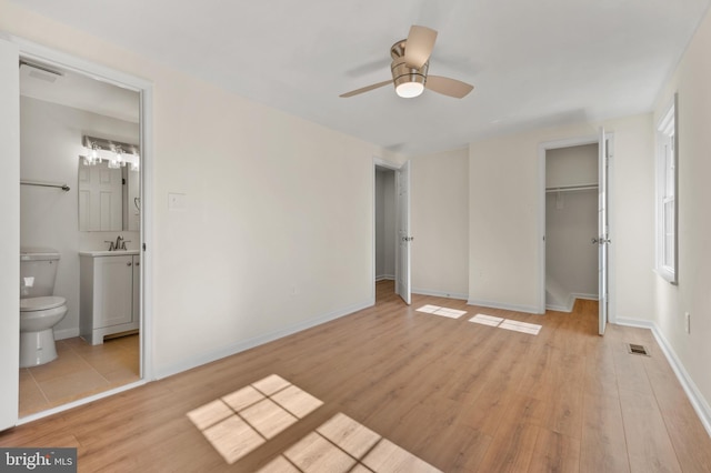 unfurnished bedroom featuring baseboards, light wood-type flooring, ensuite bathroom, a closet, and a sink