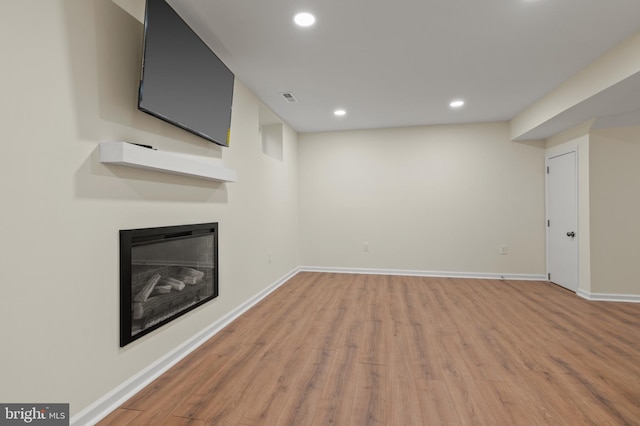 unfurnished living room featuring visible vents, wood finished floors, a glass covered fireplace, recessed lighting, and baseboards