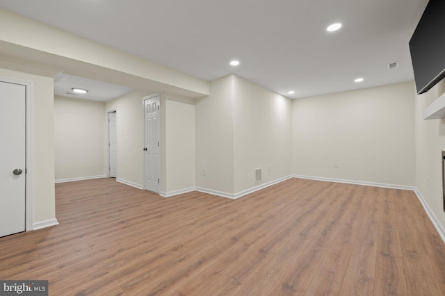 finished below grade area with a glass covered fireplace, light wood-style flooring, recessed lighting, and visible vents