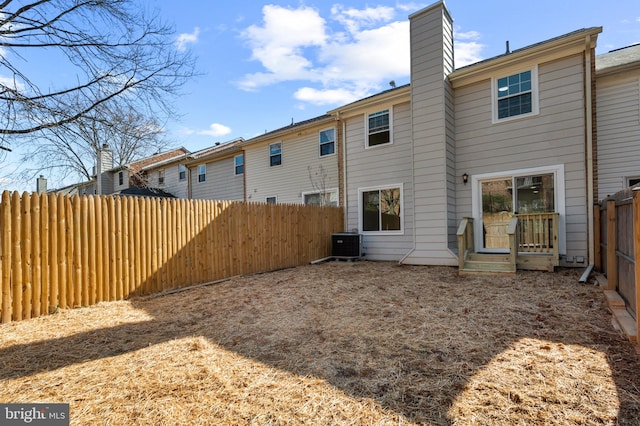 back of property with central air condition unit, a fenced backyard, and a chimney