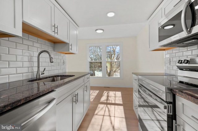 kitchen featuring dark stone countertops, a sink, stainless steel appliances, white cabinets, and light wood-type flooring