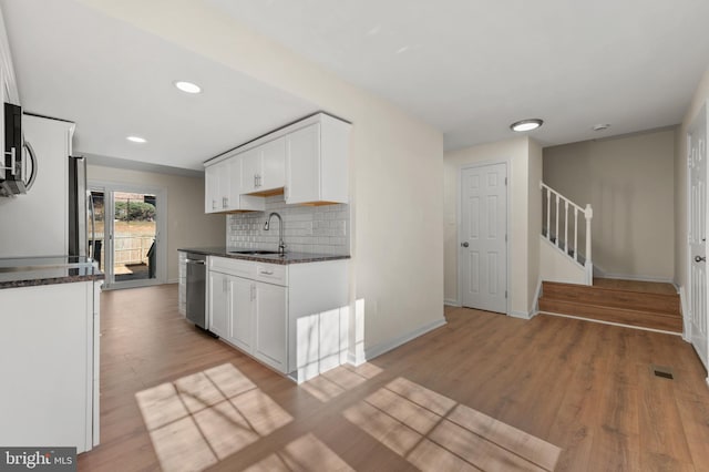 kitchen with backsplash, white cabinets, dishwasher, and light wood-style flooring