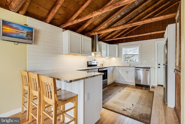 kitchen featuring stainless steel appliances, wall chimney range hood, lofted ceiling with beams, light hardwood / wood-style flooring, and white cabinetry