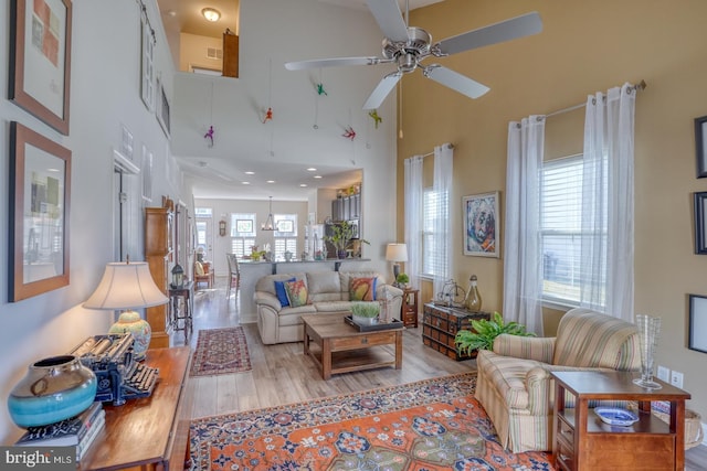 living room featuring ceiling fan, a high ceiling, and light wood-type flooring