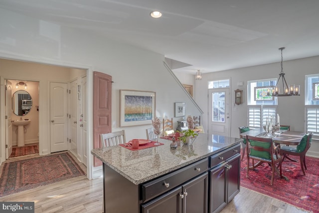 kitchen with light stone countertops, a center island, decorative light fixtures, and light hardwood / wood-style floors