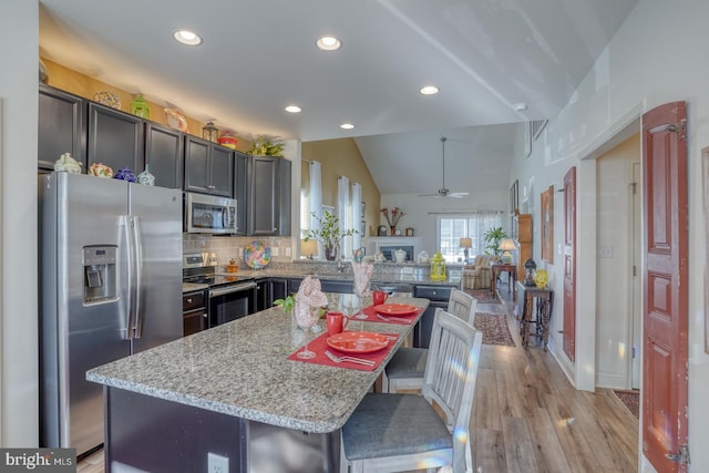 kitchen with appliances with stainless steel finishes, light stone counters, a breakfast bar area, a center island, and lofted ceiling