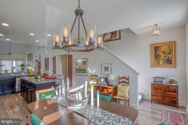 dining room with ceiling fan with notable chandelier, light wood-type flooring, and sink