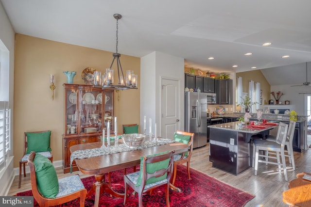 dining area with ceiling fan with notable chandelier, light wood-type flooring, and lofted ceiling