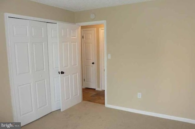 unfurnished bedroom featuring light carpet, a textured ceiling, and a closet